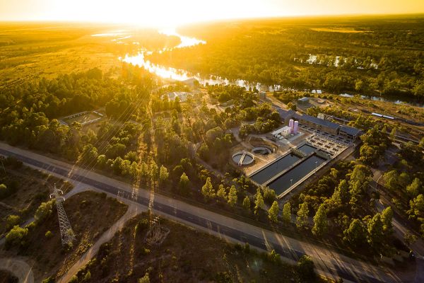 An aerial shot of Morgan Water Treatment Plant, set in between rows of trees. Behind the Treatment Plant is the River Murray, and a glowing orange sunset.